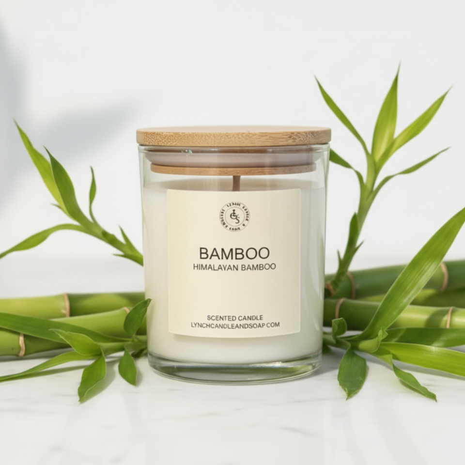 Scented candle labeled 'Bamboo' with a wooden lid, surrounded by bamboo leaves on a light background.