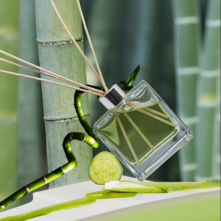 Reed diffuser with bamboo sticks and a cucumber slice on a white platform with a bamboo background